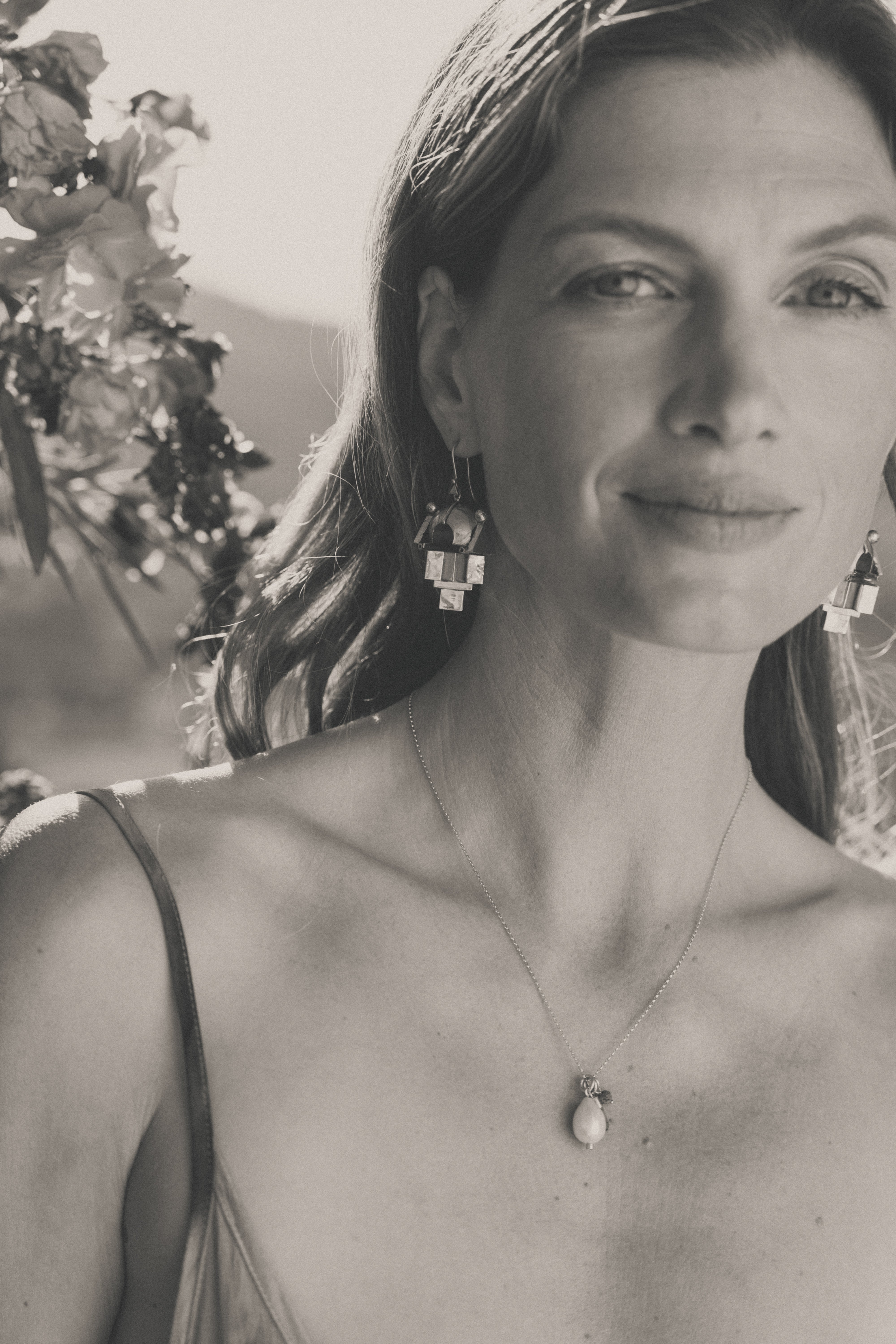 A model wearing vintage gold Thandatti tribal drop earrings with flowers in the background. Image in black & white