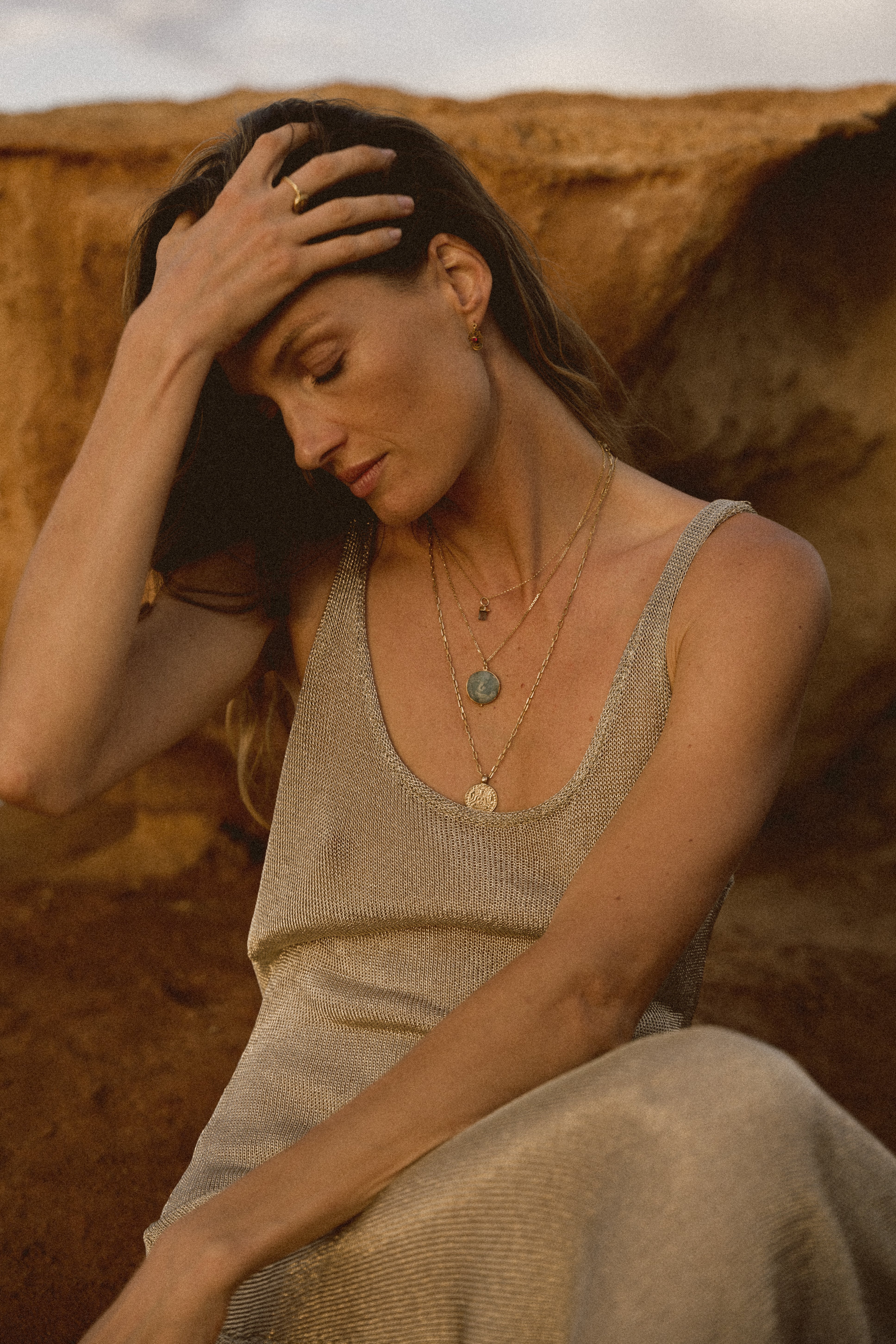A model in a gold dress wearing the vintage gold flower earrings and gold necklaces sat against a desert backdrop