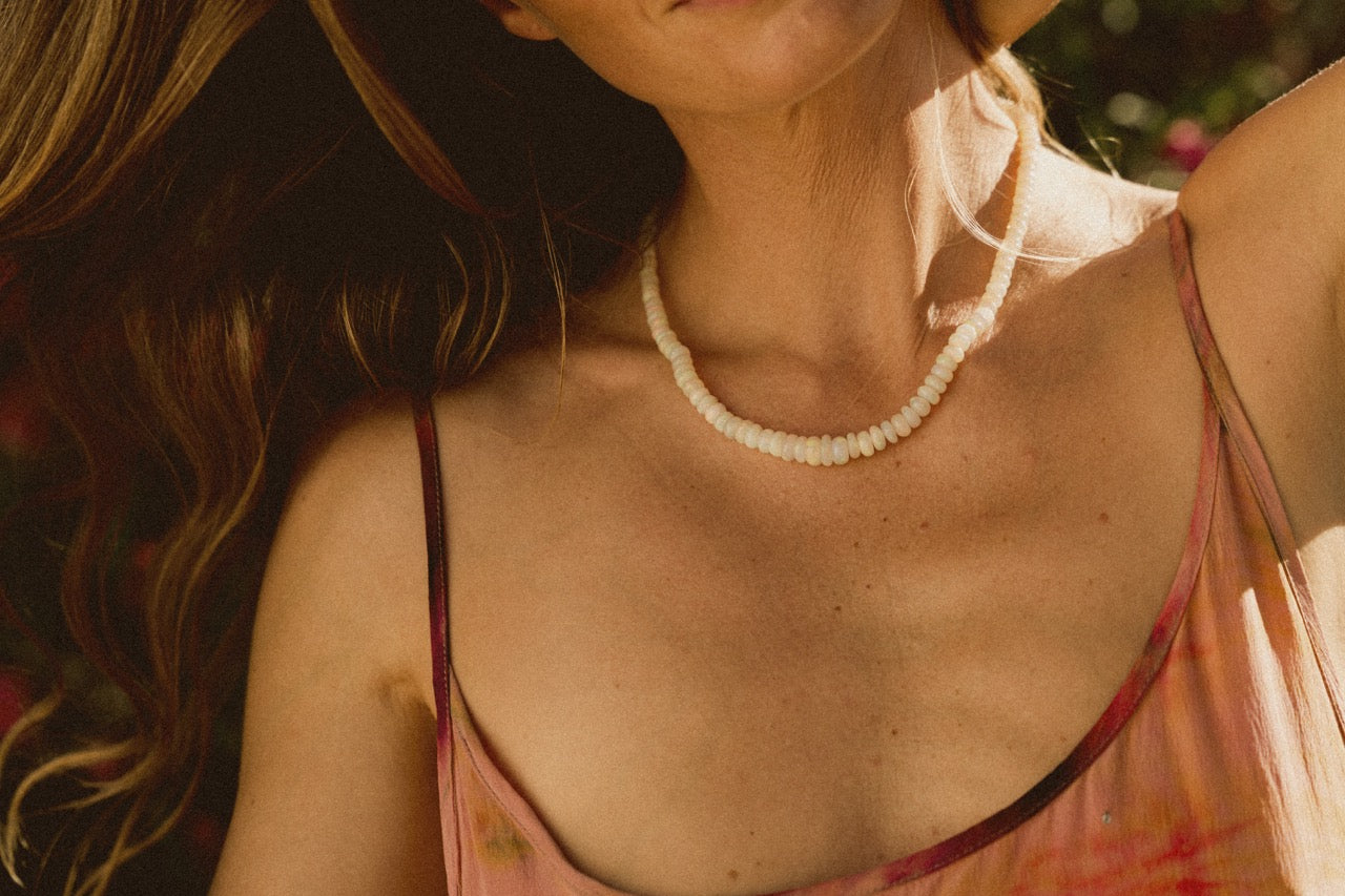 A woman wearing a pink floral dress and a beaded opal necklace with a gold clasp 