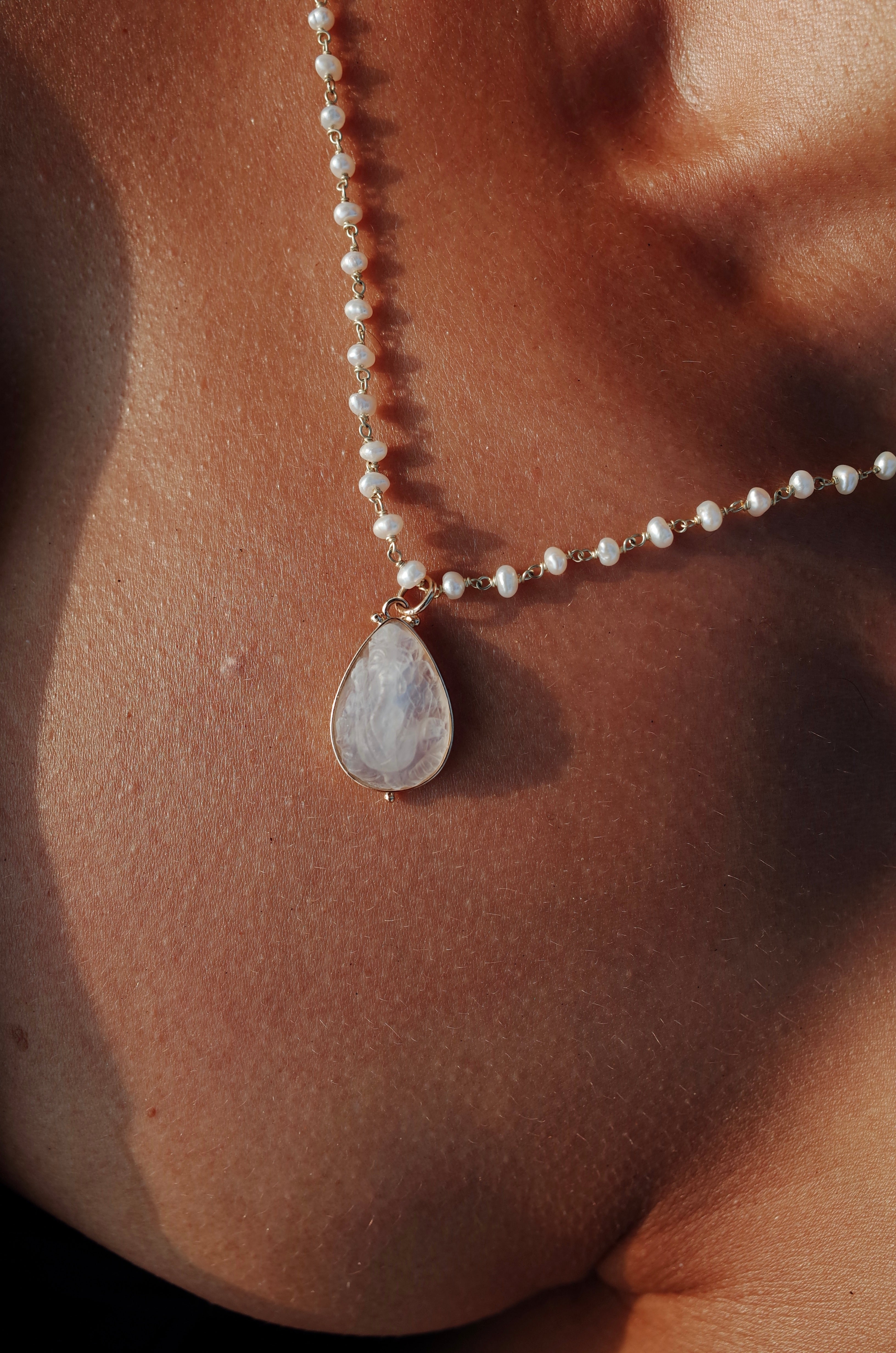 A close-up image of a model wearing a beaded pearl necklace with a rainbow moonstone Ganesha pendant