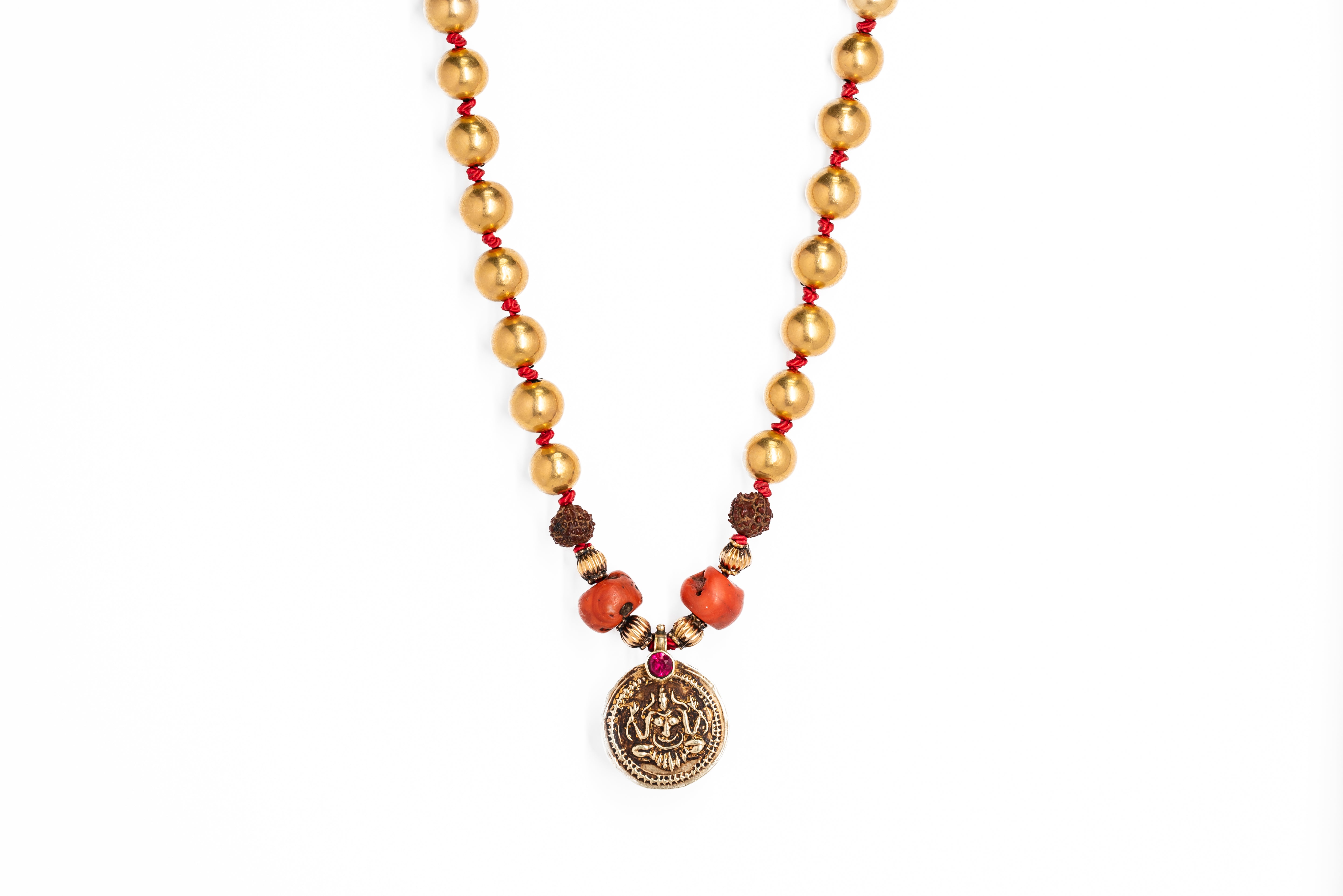 A gold bead necklace with a central amulet depicting 'Yellama Devi', with red coral and gold against a white background