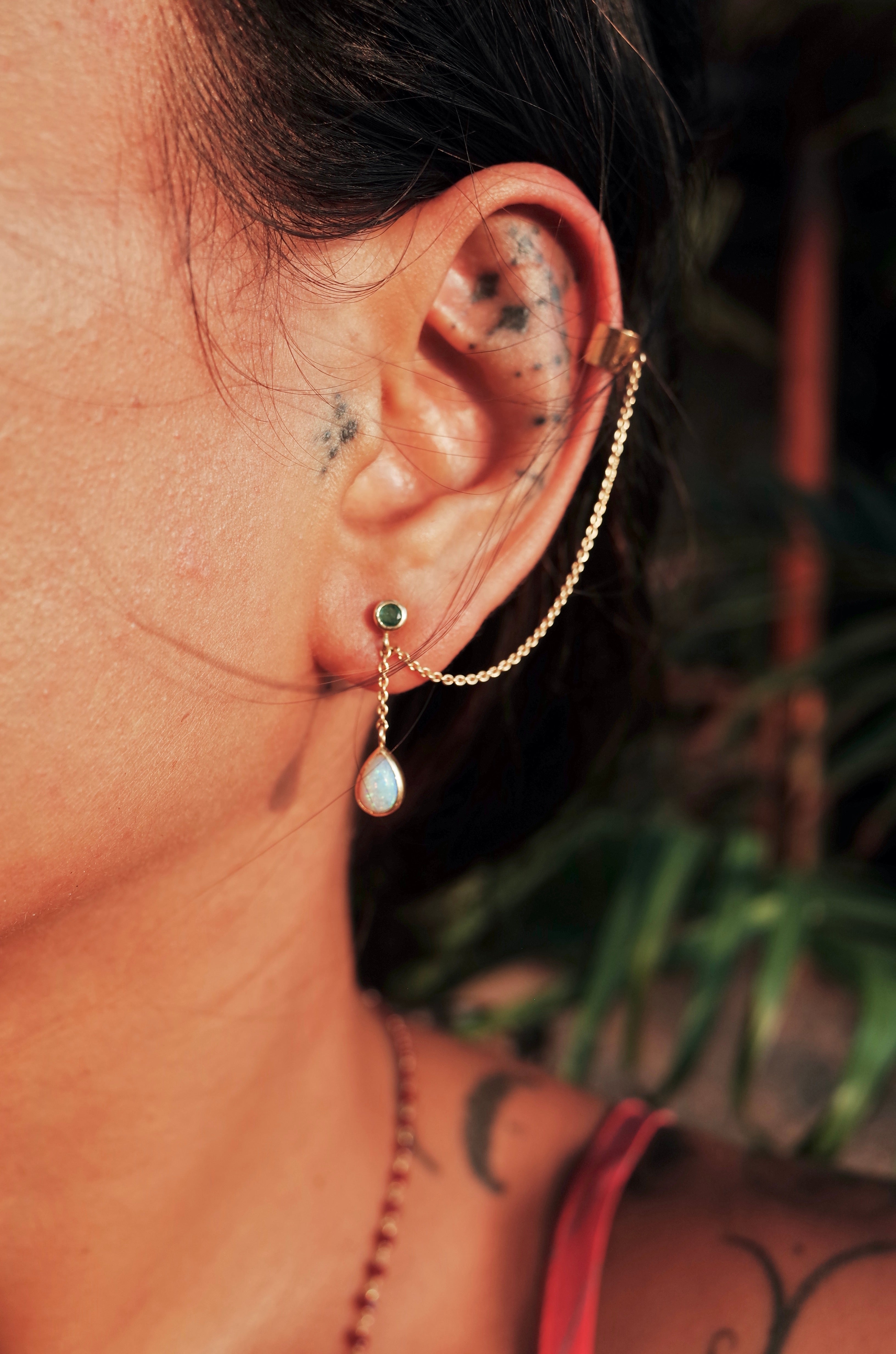 Close up of a models' ear featuring the emerald and diamond earcuff in 18ct gold