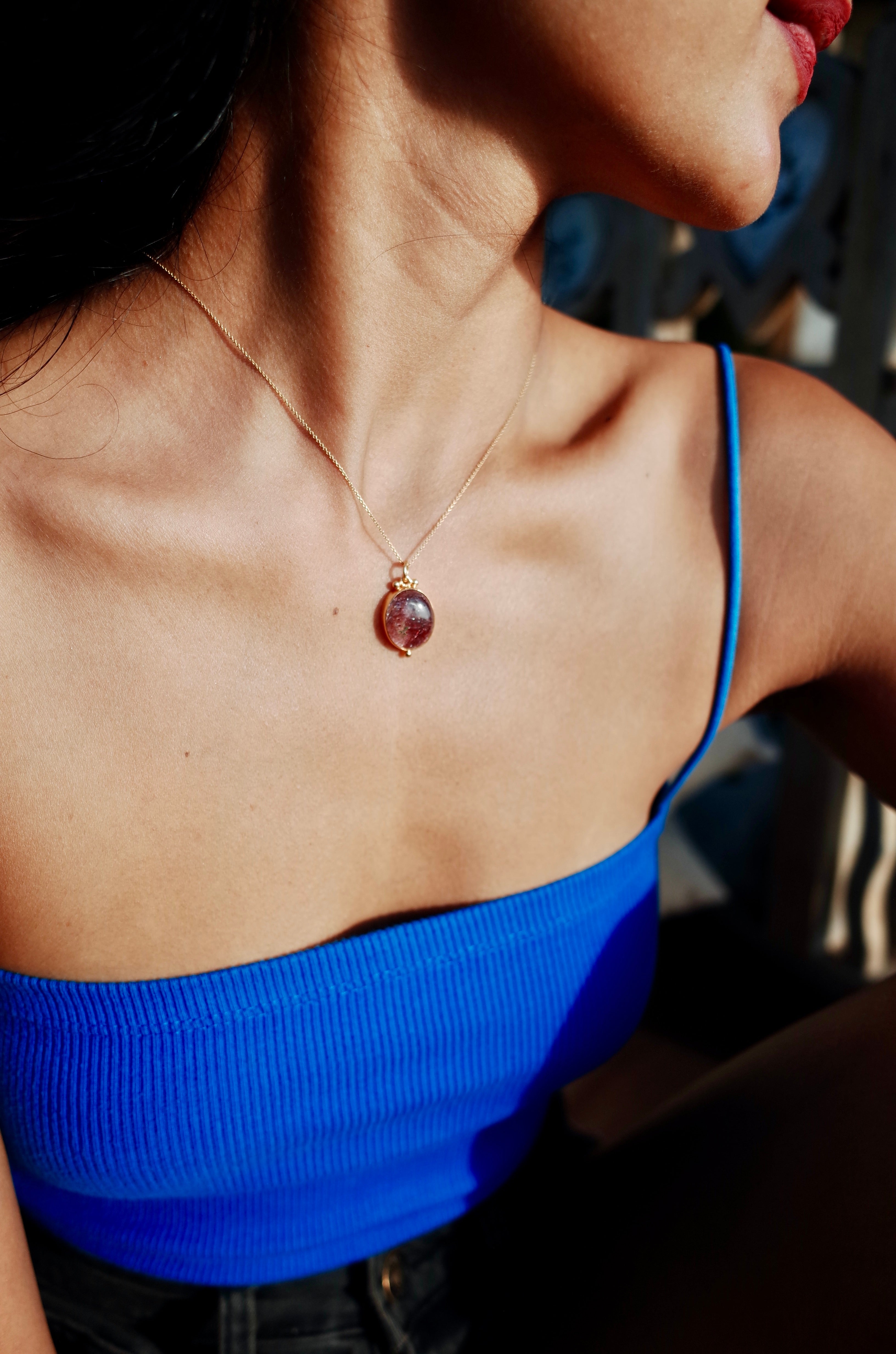 A model wearing a blue sleeveless top and a Super Seven crystal amulet pendant.