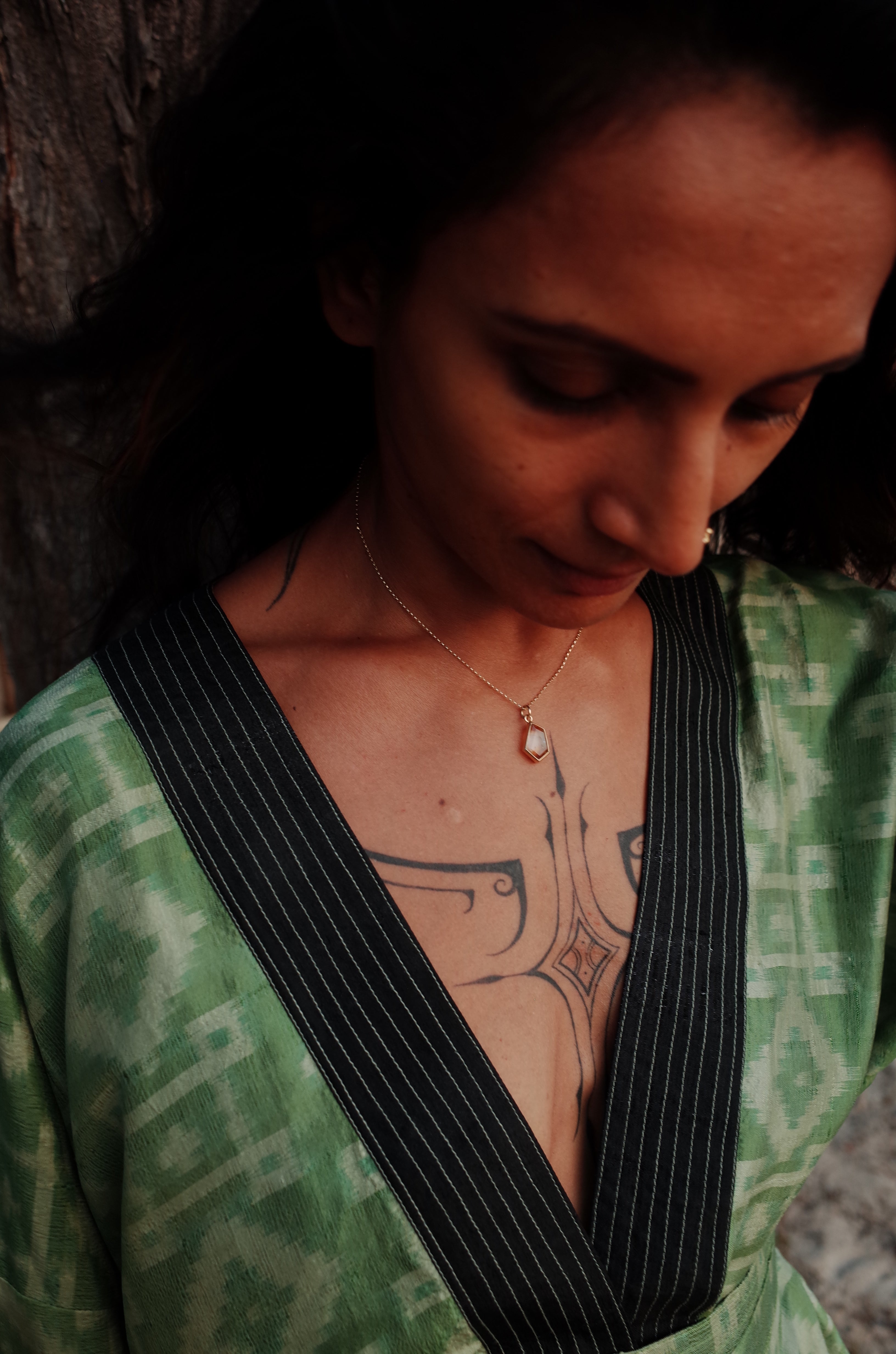 A tattooed model wearing a green and black v-neck shirt and the citrine window amulet necklace 