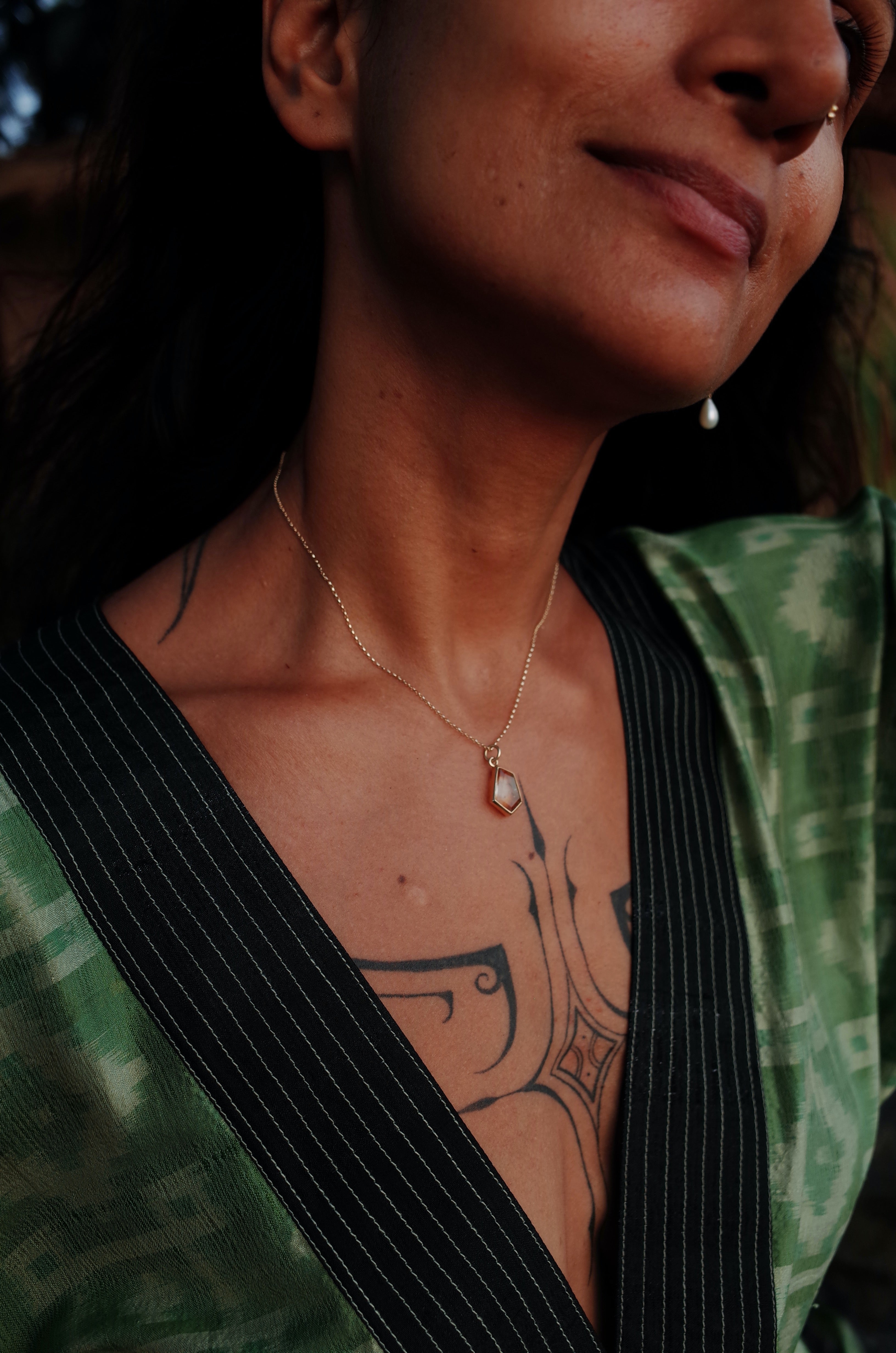 A tattooed model wearing a green and black shirt with the citrine window amulet necklace 