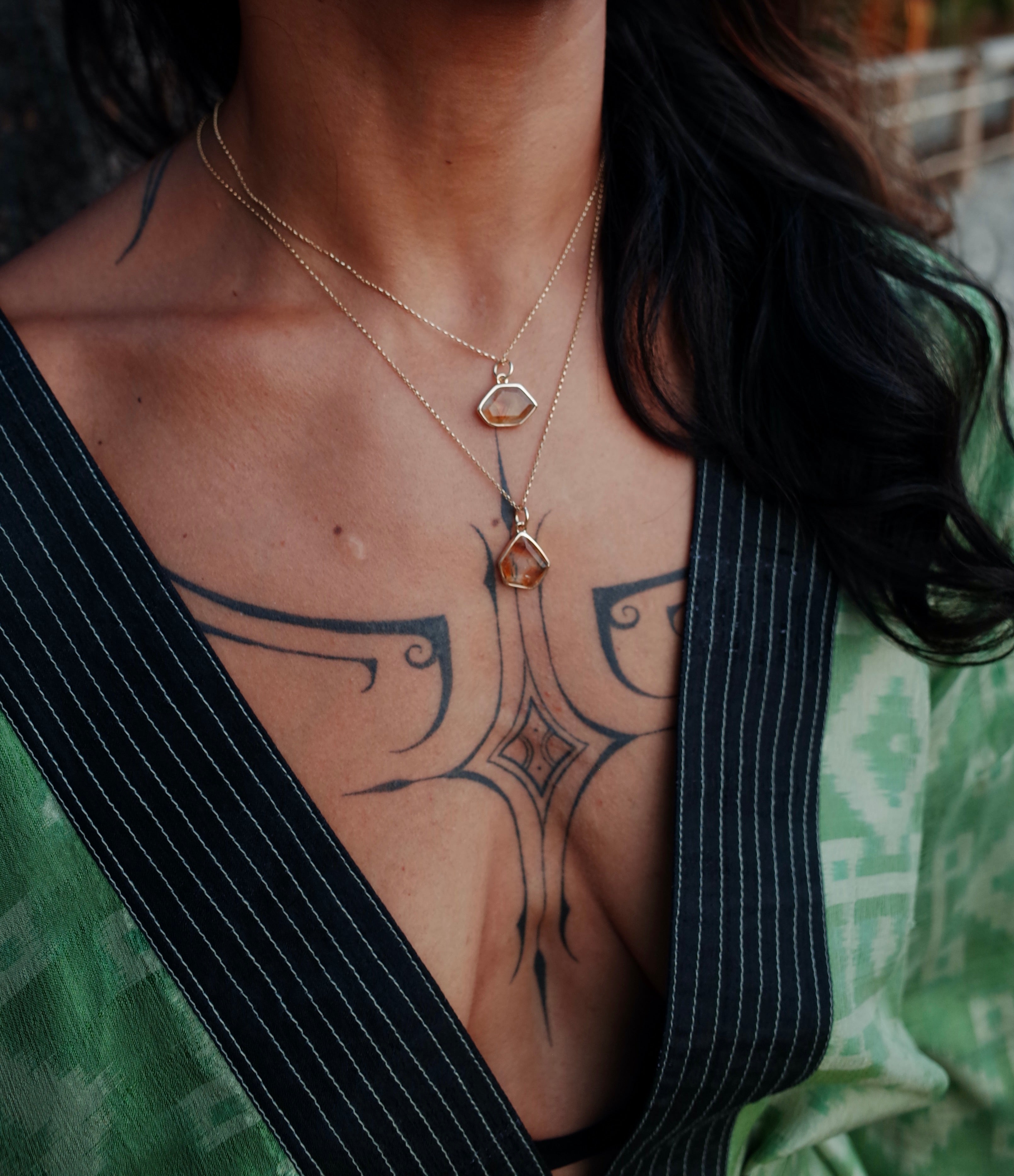 The tattooed chest of a model wearing a citrine window amulet necklace on a gold chain