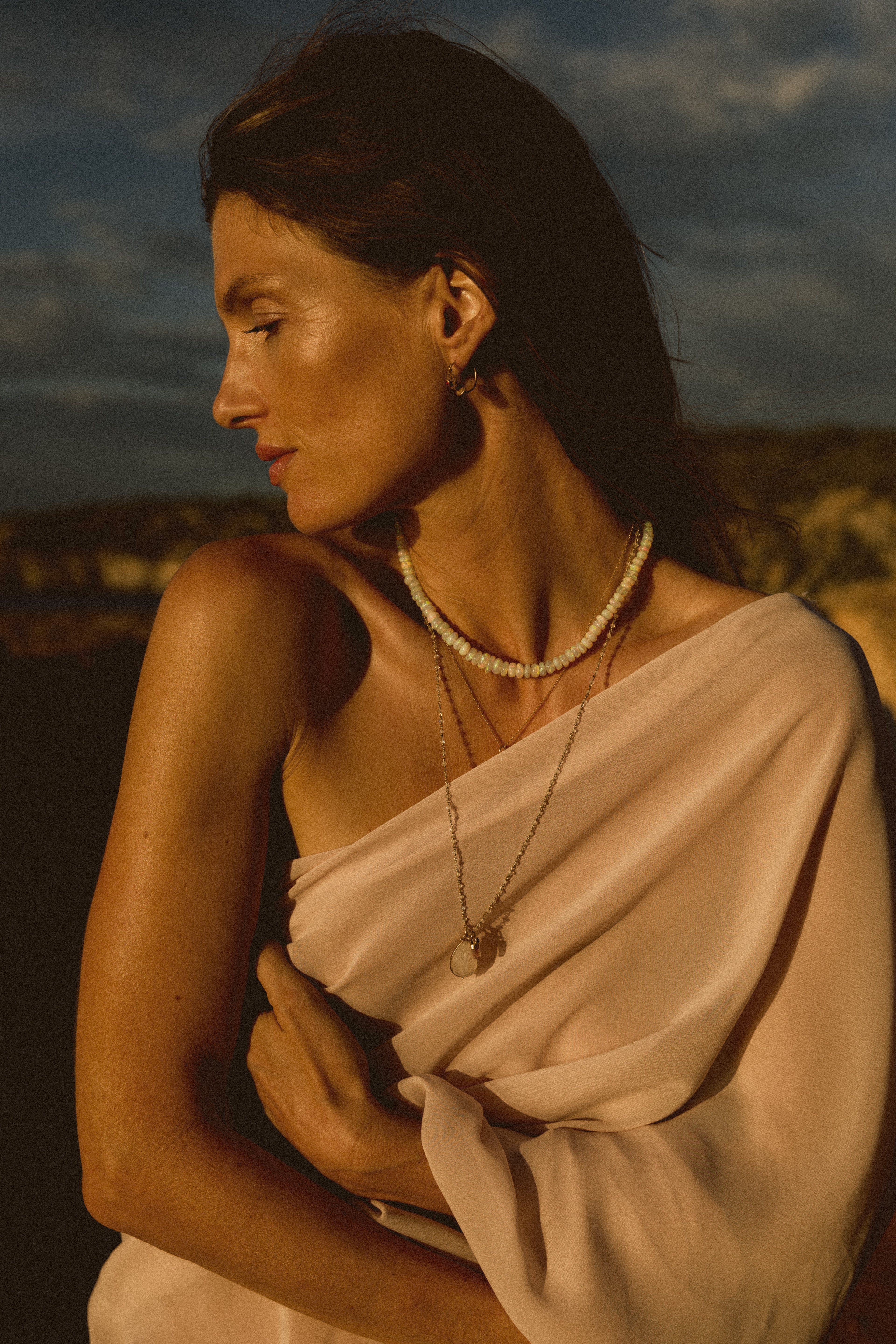 A model in a pink dress looking to the side wearing vintage gold flower earrings with hills in the background