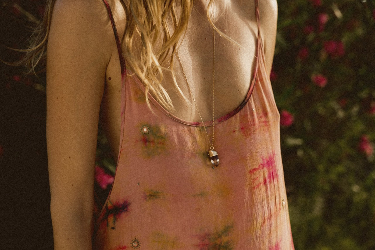 A model shown from the below the shoulders wearing a pink dress and a red phantom quartz amulet pendant