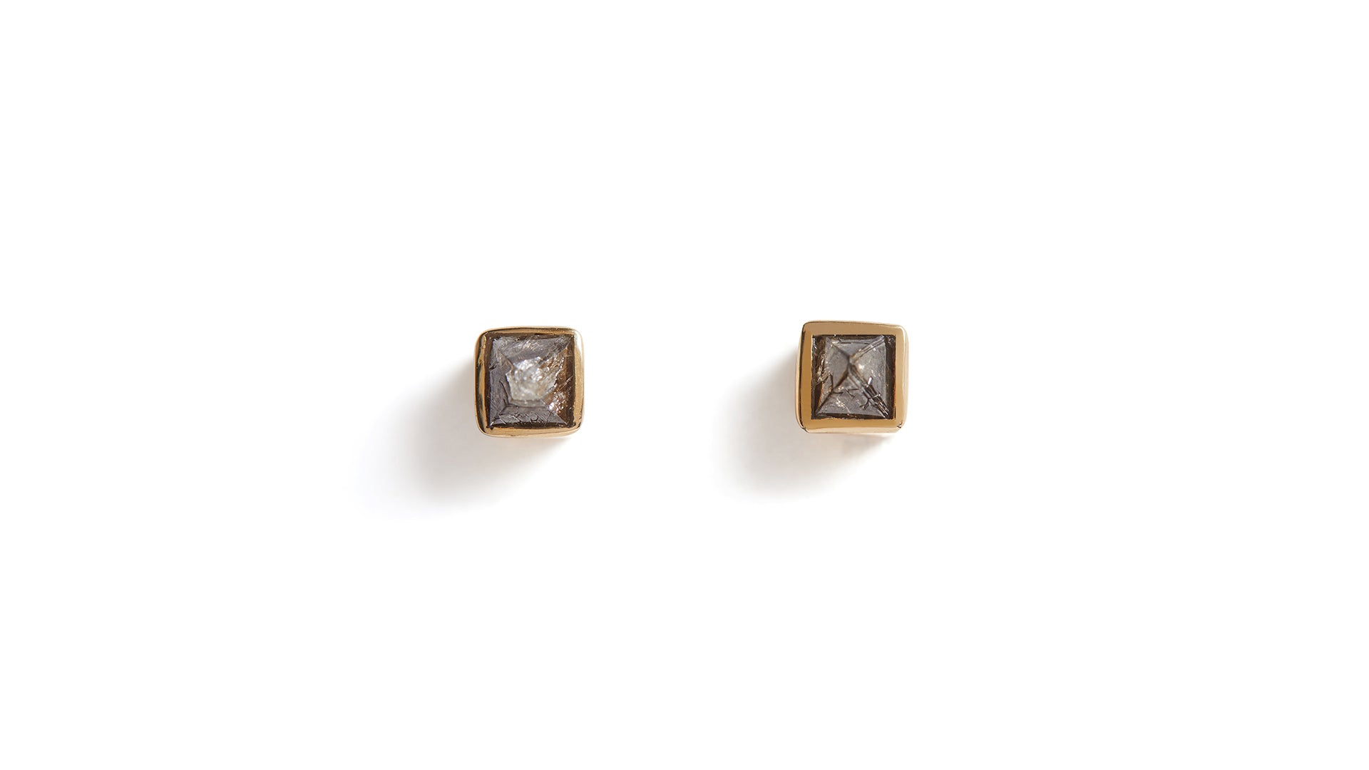 A pair of raw diamond gold studs against a white background