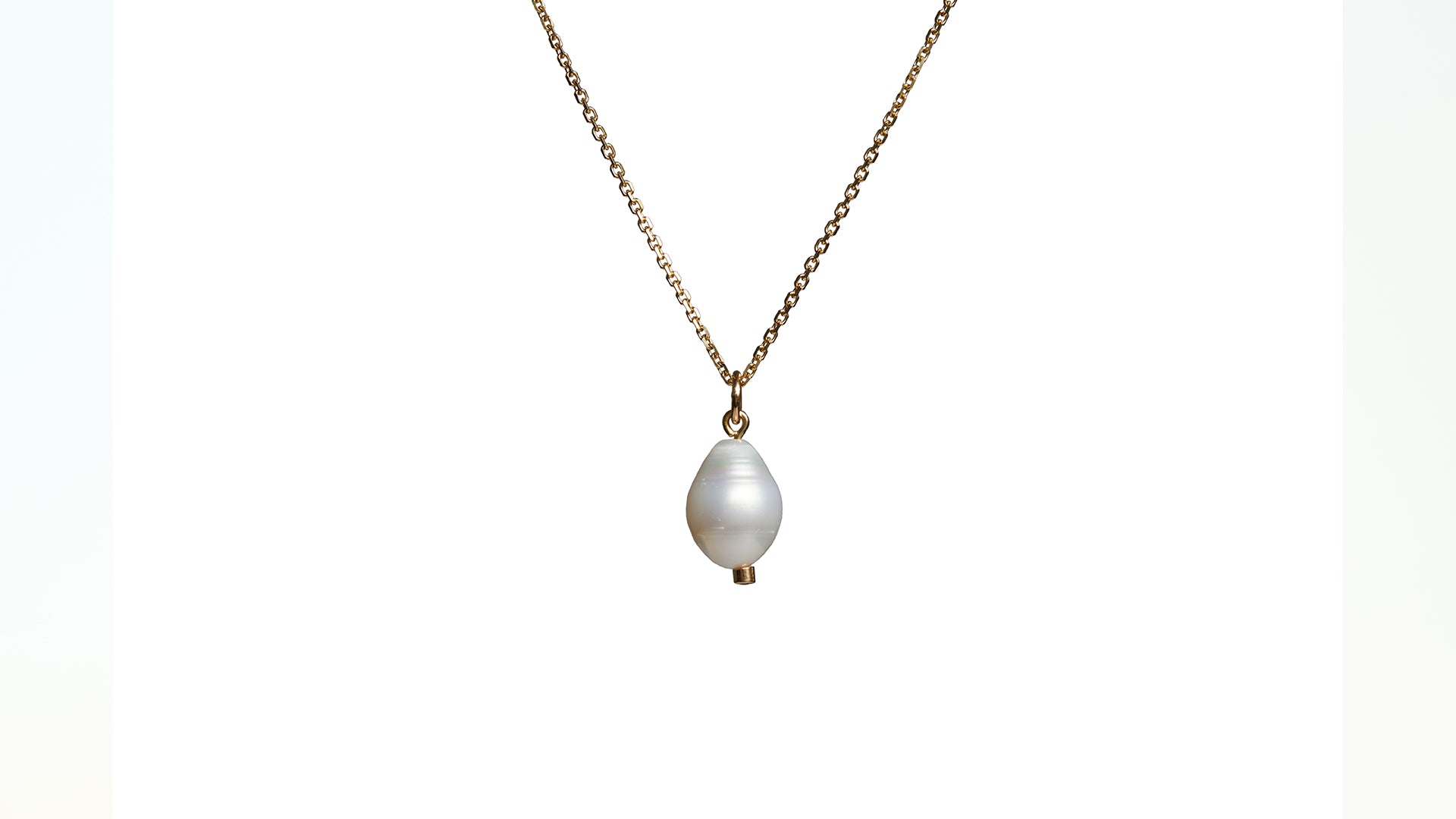 A pearl and orange sapphire charm pendant on a gold chain against a white background